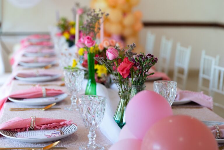 A beautifully decorated party table with pink accents, flowers, and glassware.